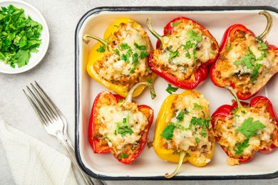 A dish of stuffed bell peppers topped with melted cheese and parsley garnish on a tray served with a fork and parsley on the side