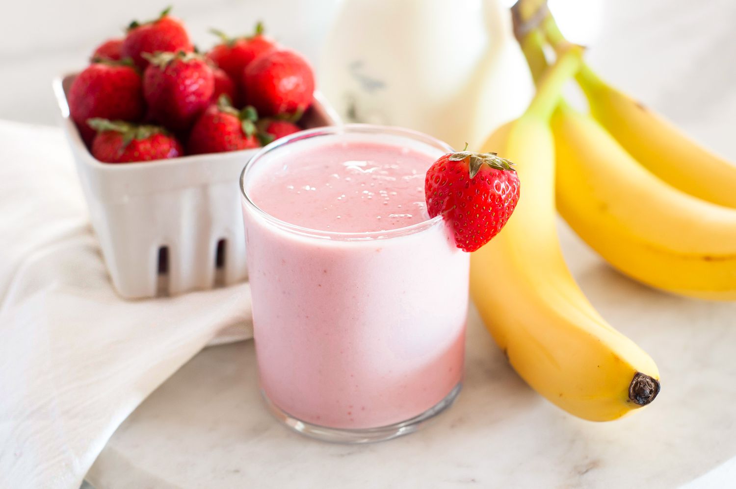 A glass with a strawberry banana smoothie and strawberry and banana fruits in the background