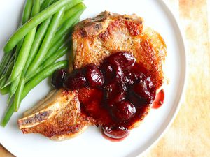 Overhead view of a a stove top pork chop topped with cherry sauce with a side of green beans.
