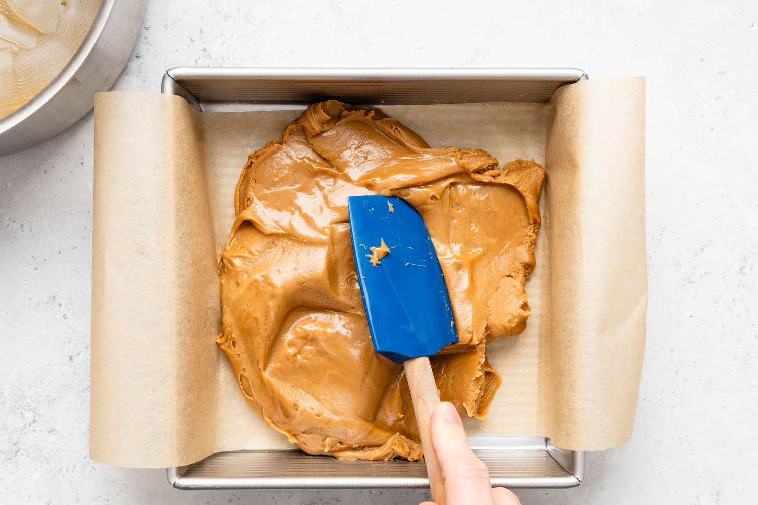 Penuche mixture transfered to parchment paper-lined baking pan and flattened using a rubber spatula