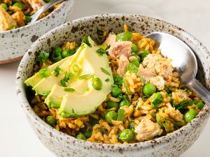 A bowl of rice mixed with peas salmon and topped with avocado slices served with a spoon