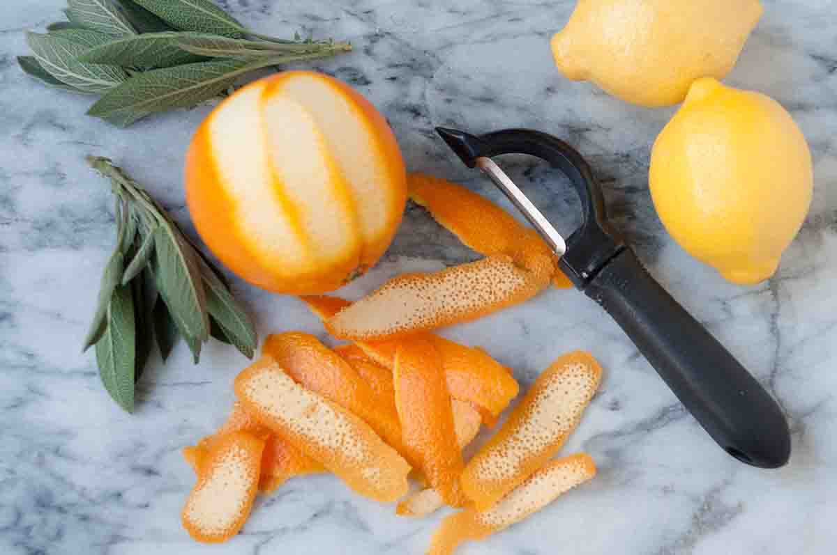 A peeled orange, sage, and lemons on a marble board
