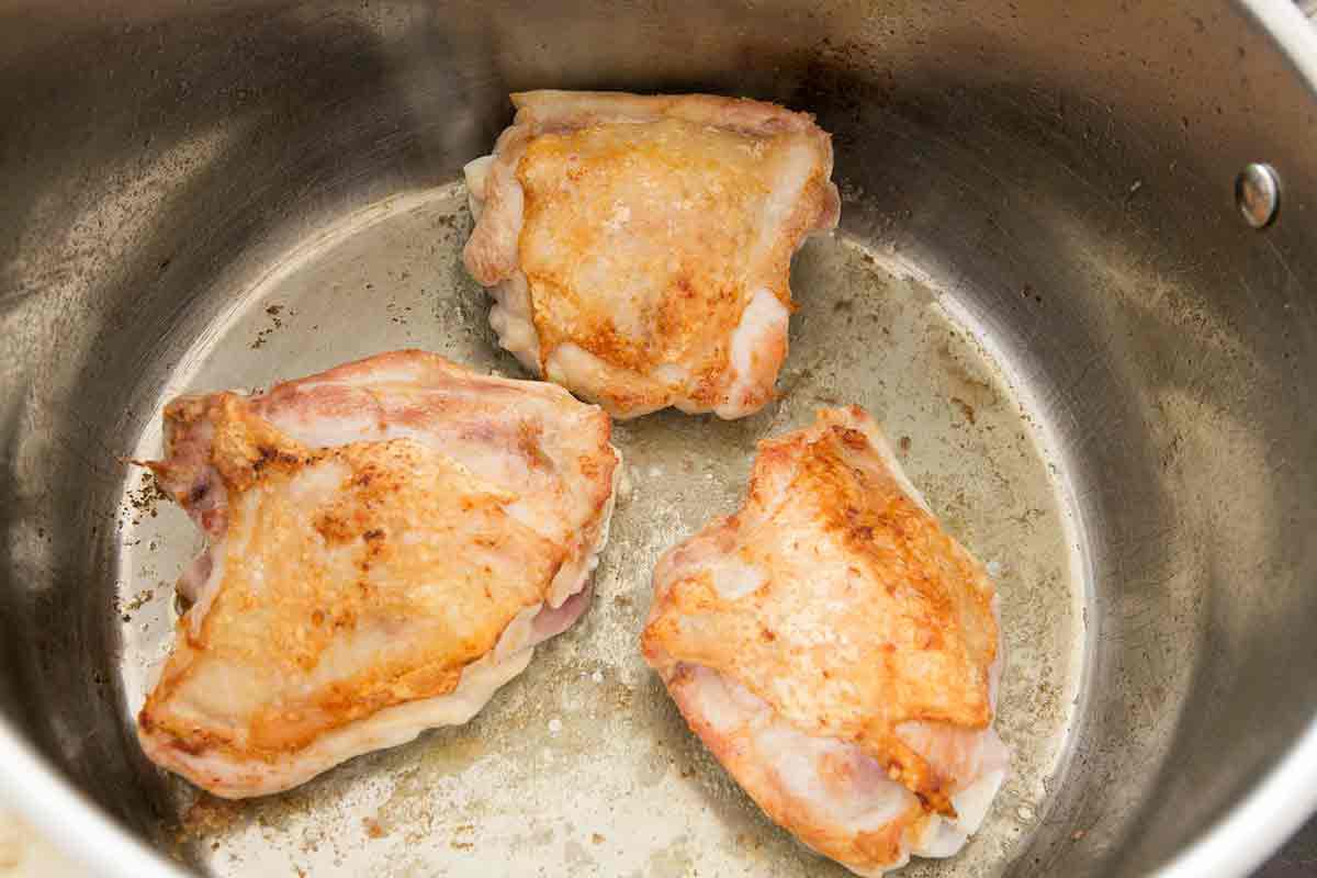 Skin-on chicken browning in a stock pot for chicken dumplings.