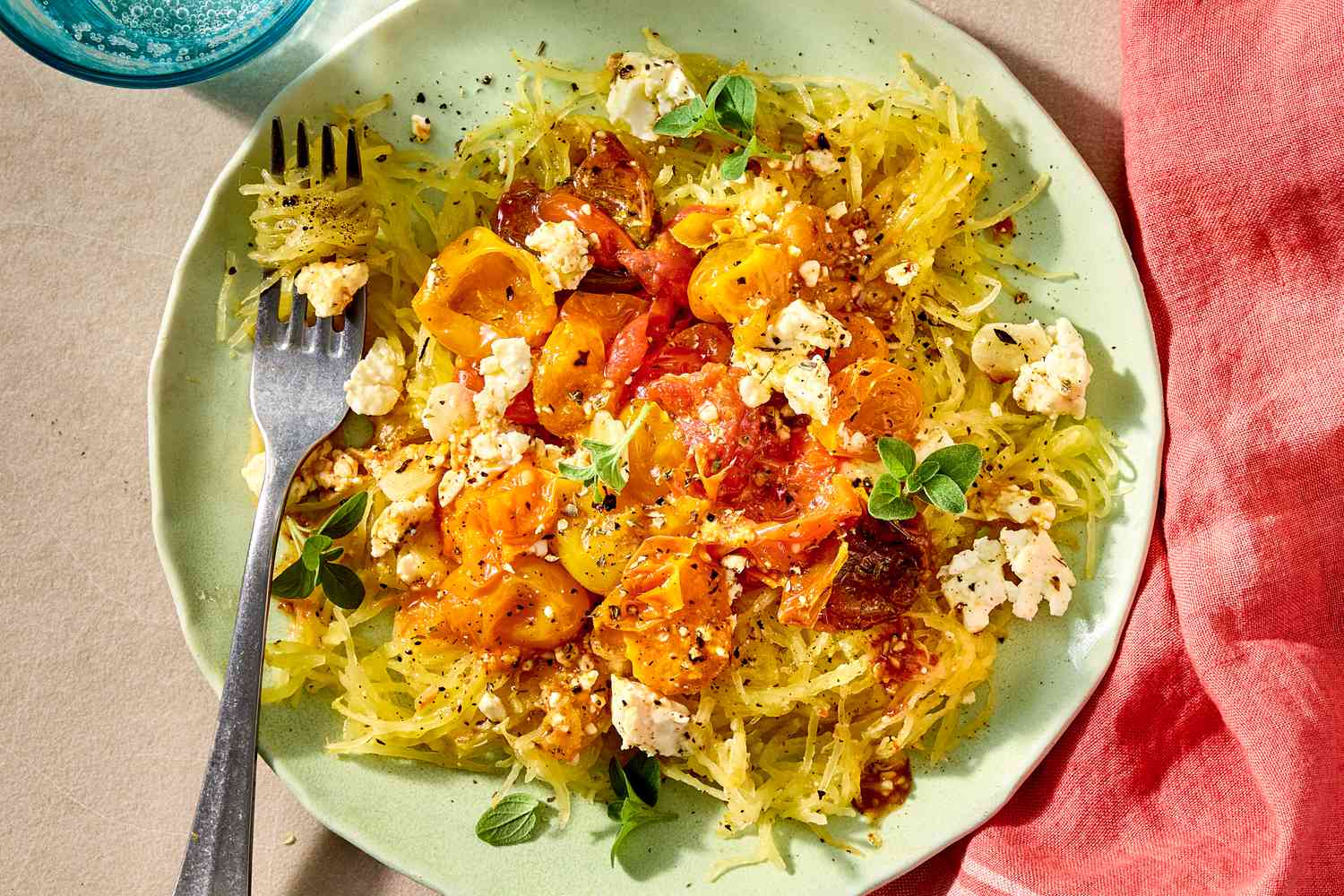 Overhead view of a plate with spaghetti squash topped with feta and cherry tomatoes, with a fork holding some of the squash
