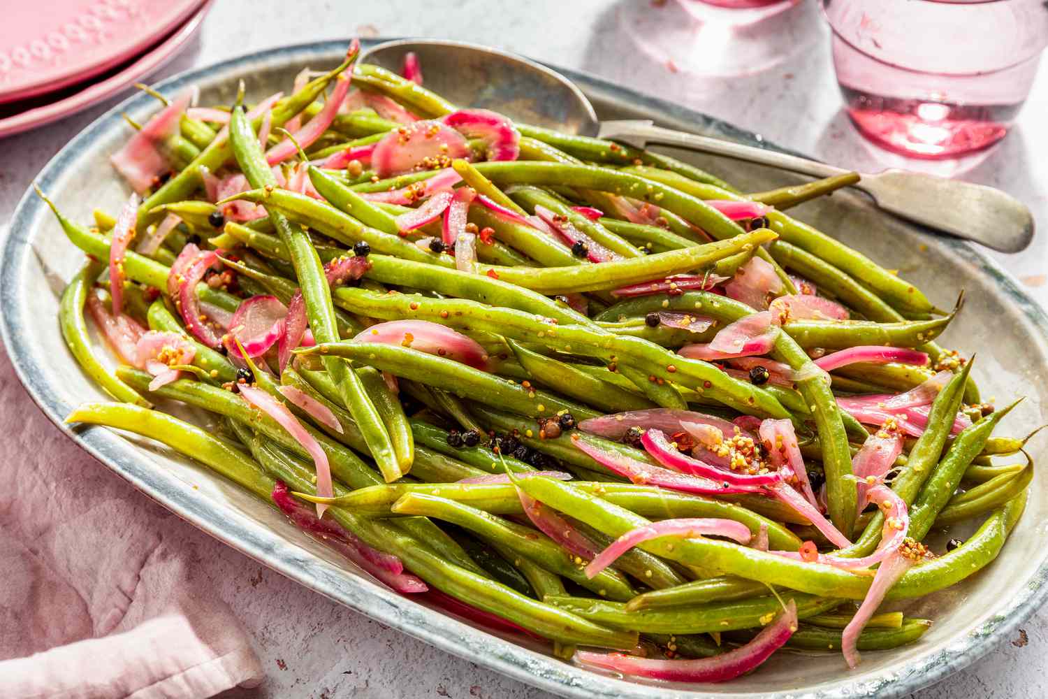 pickled green beans on a platter next to a glass of water and a stack of plates