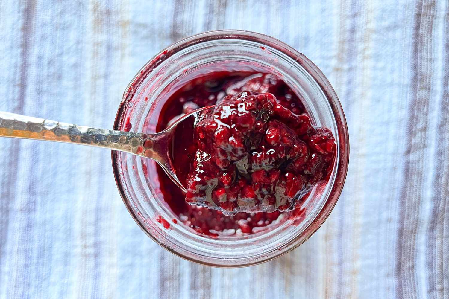 An open jar of marionberry jam with a spoon in it
