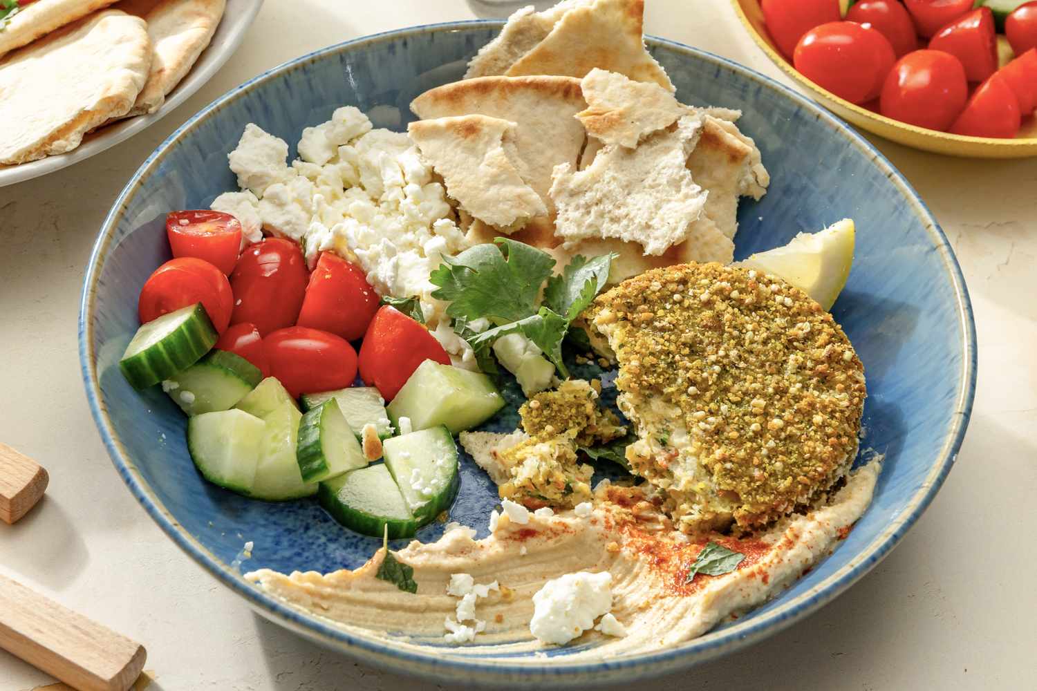 overhead view of Falafel Bowl - pita, feta, falafel, hummus, lemon slice, cucumbers, and grape tomatoes