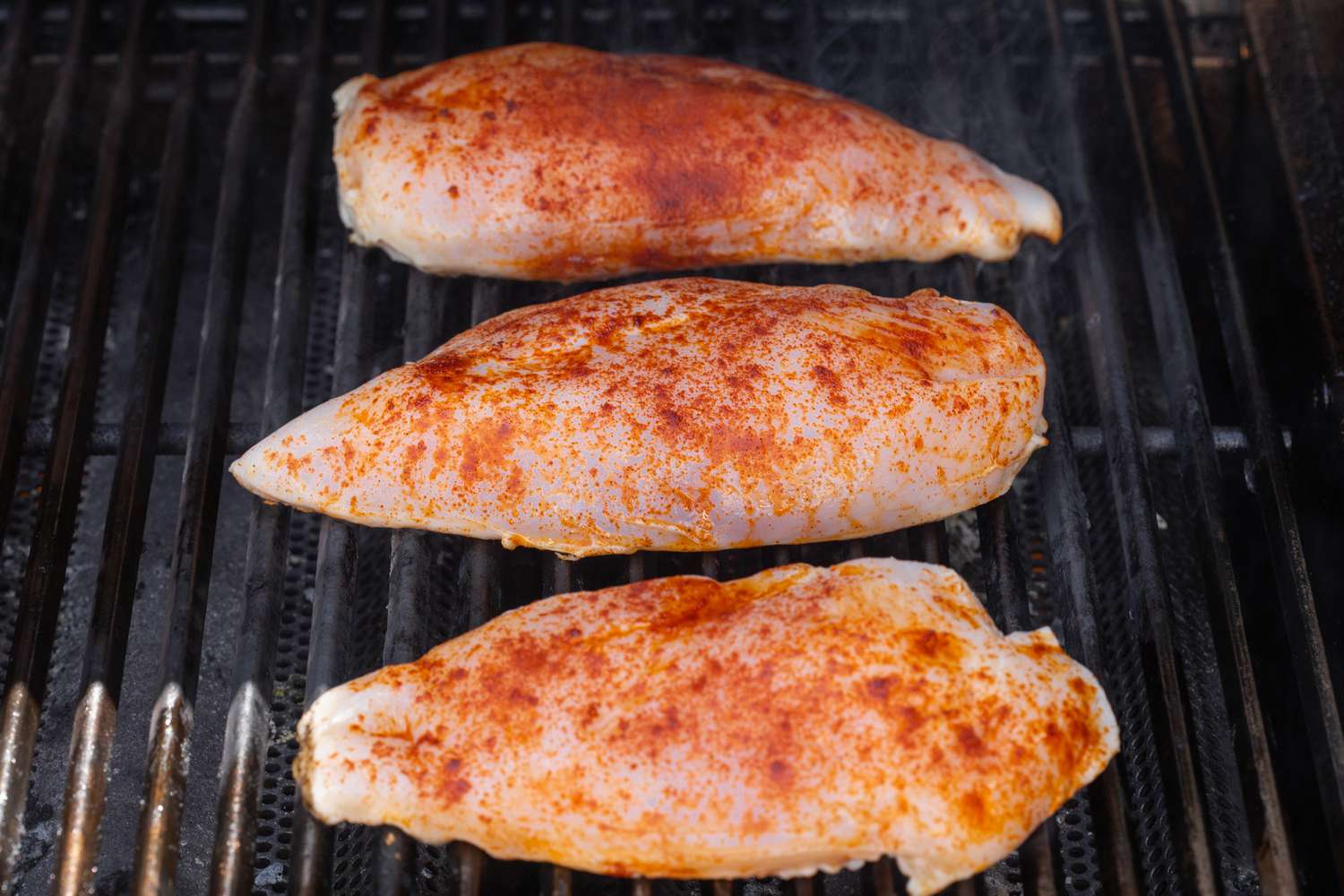 Three chicken breasts on a grill to show how long to grill chicken.