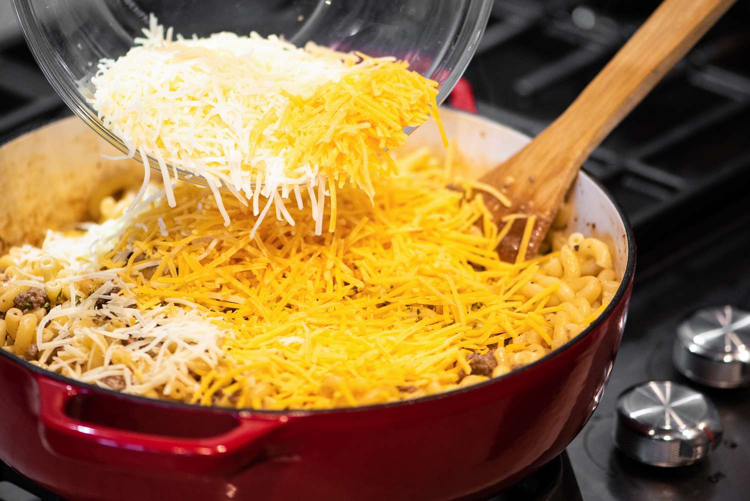 Large Bowl of Monterey Jack Cheese and Cheddar Cheese Added to Cheeseburger Casserole Ingredients in Dutch Oven 