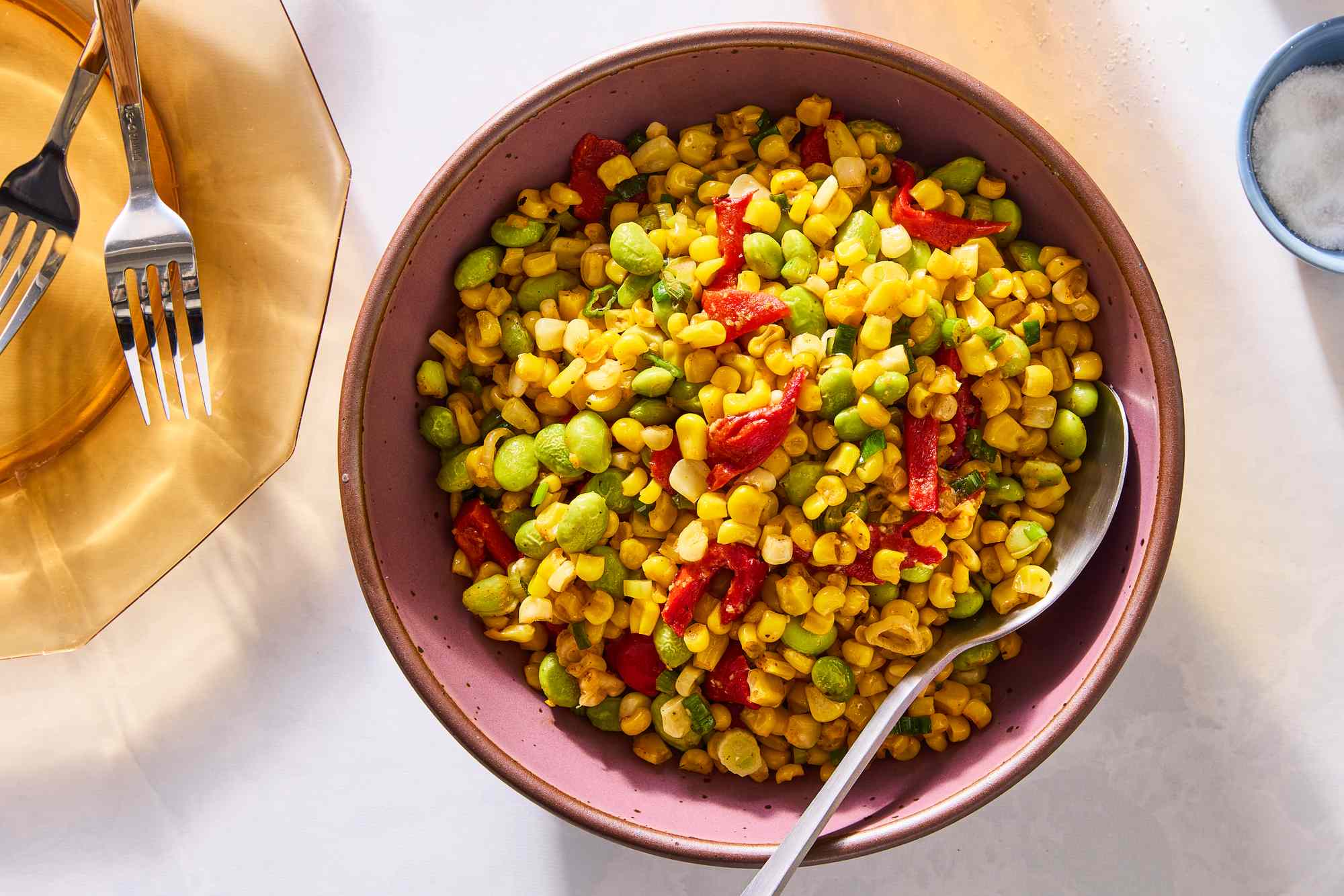 A bowl of Thanksgiving succotash with a serving spoon on a white table