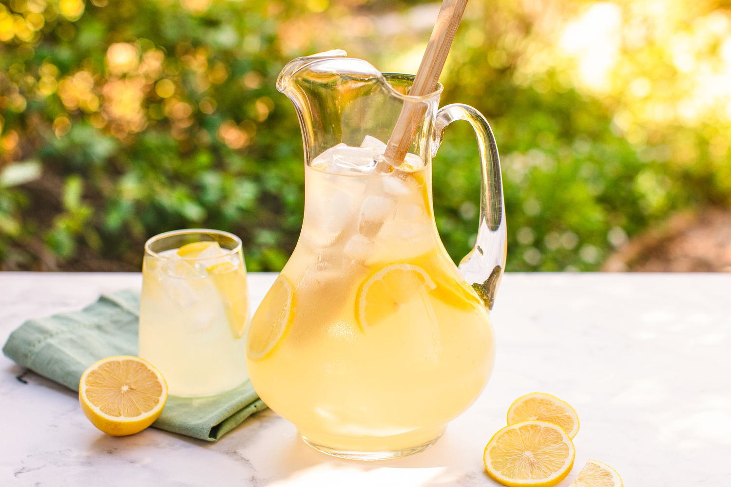 A pitcher and a glass filled with lemonade placed on a table, garnished with lemon slices