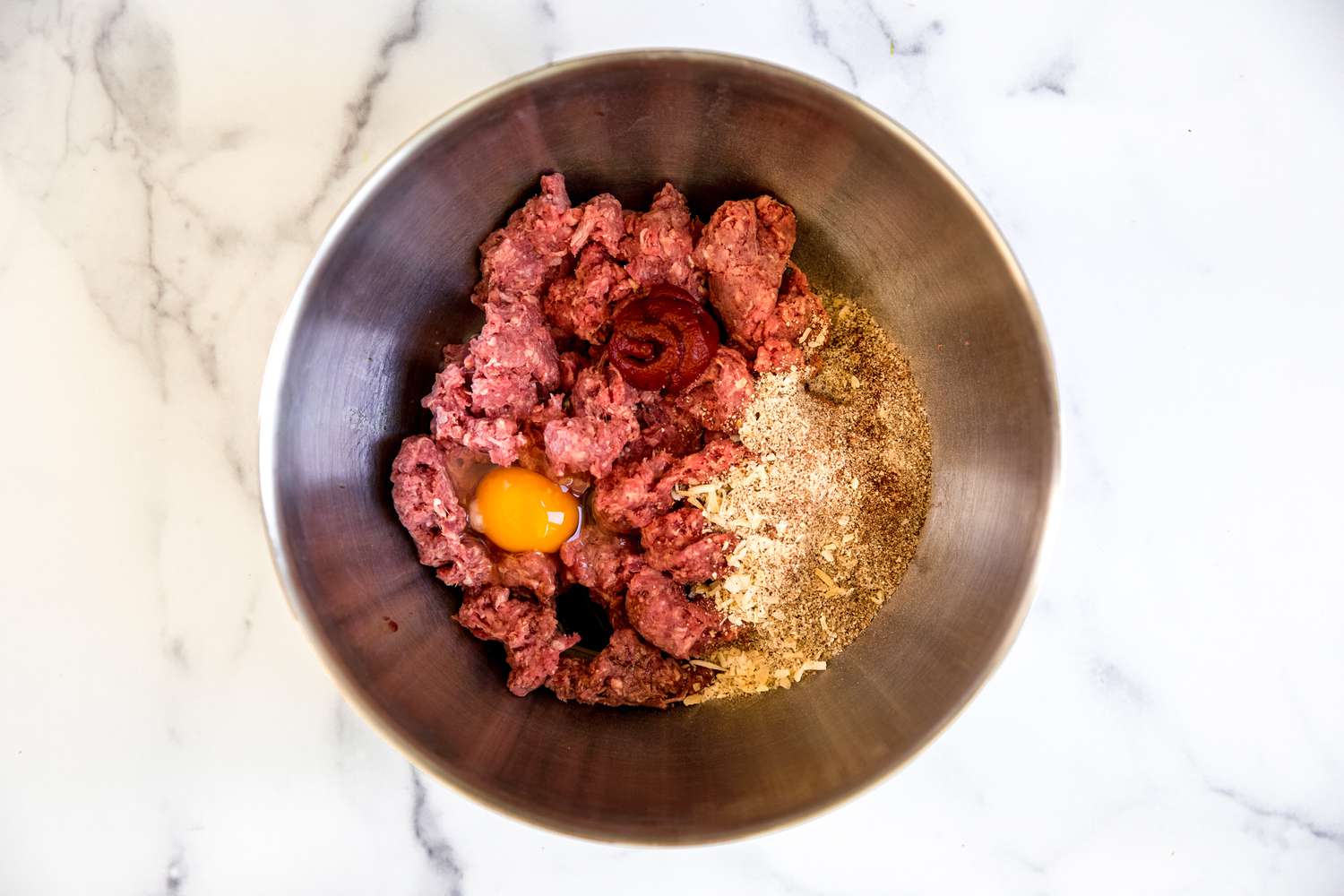 Meat, egg, and dry ingredients in a bowl to make mini meatloaves with veg and potatoes in a sheet pan.