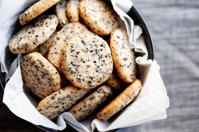 Buttery sesame cookies in a cookie tin lined with white tissue paper. 