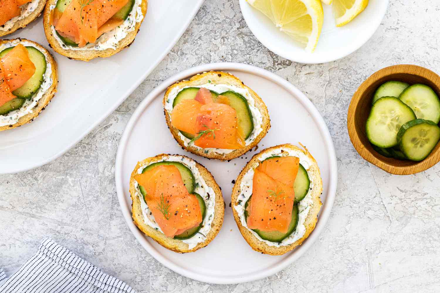 Overhead view of three smoke salmon and herby cream cheese crostinis on a plate with lemon next to it. 