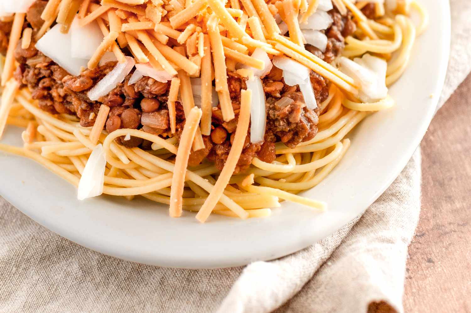 Vegan Cincinnati Chili Served over a Platter of Pasta and Topped with Cheese and Onions