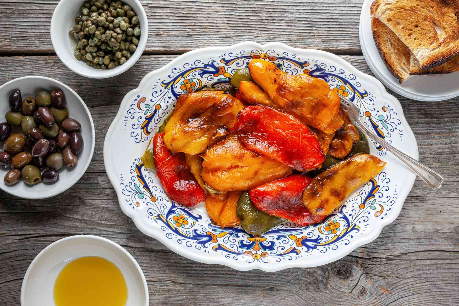 Platter of Grilled Peppers Surrounded by Olives, Capers, Olive Oil, and Toast