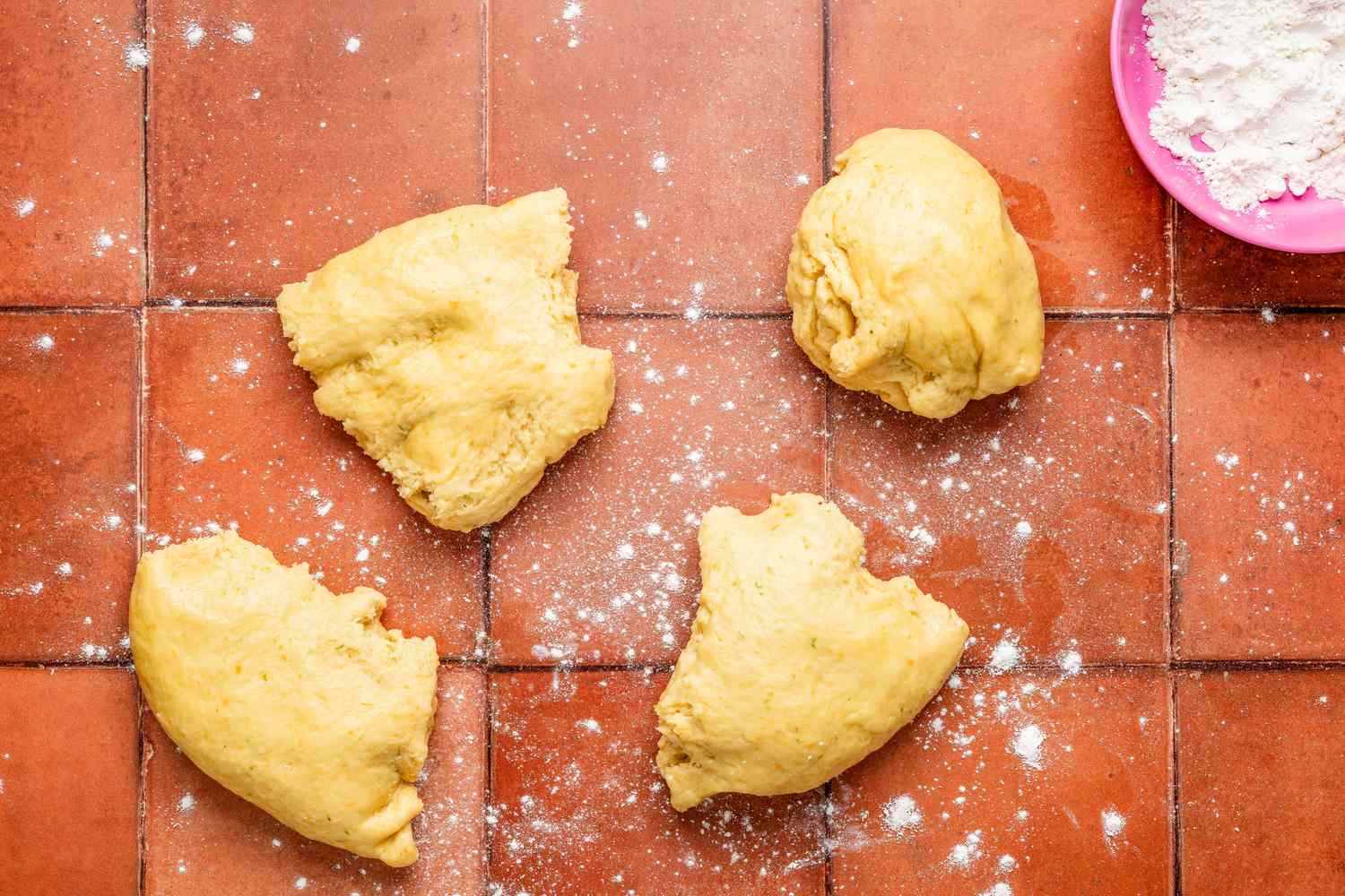Pan de muerto dough divided into 4 equal portions on a light dusted surface