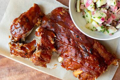bbq ribs on a plate next to a bowl of potato salad 