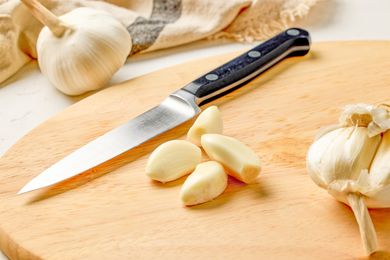 Garlic cloves and a knife on a wooden cutting board