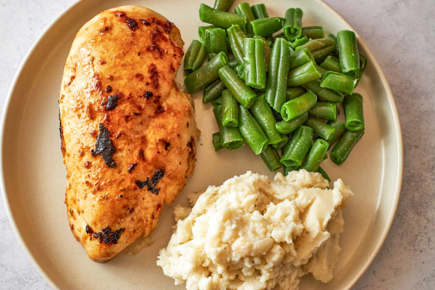 Overhead shot of a plate with a marinated and cooked chicken breast, green beans and mashed potato on a a plate