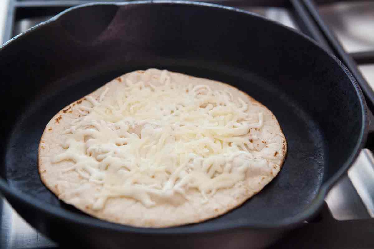 sprinkle cheese on tortilla in cast iron pan to make tortilla pizza