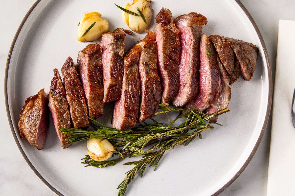 Sliced steak on a plate with rosemary and garlic