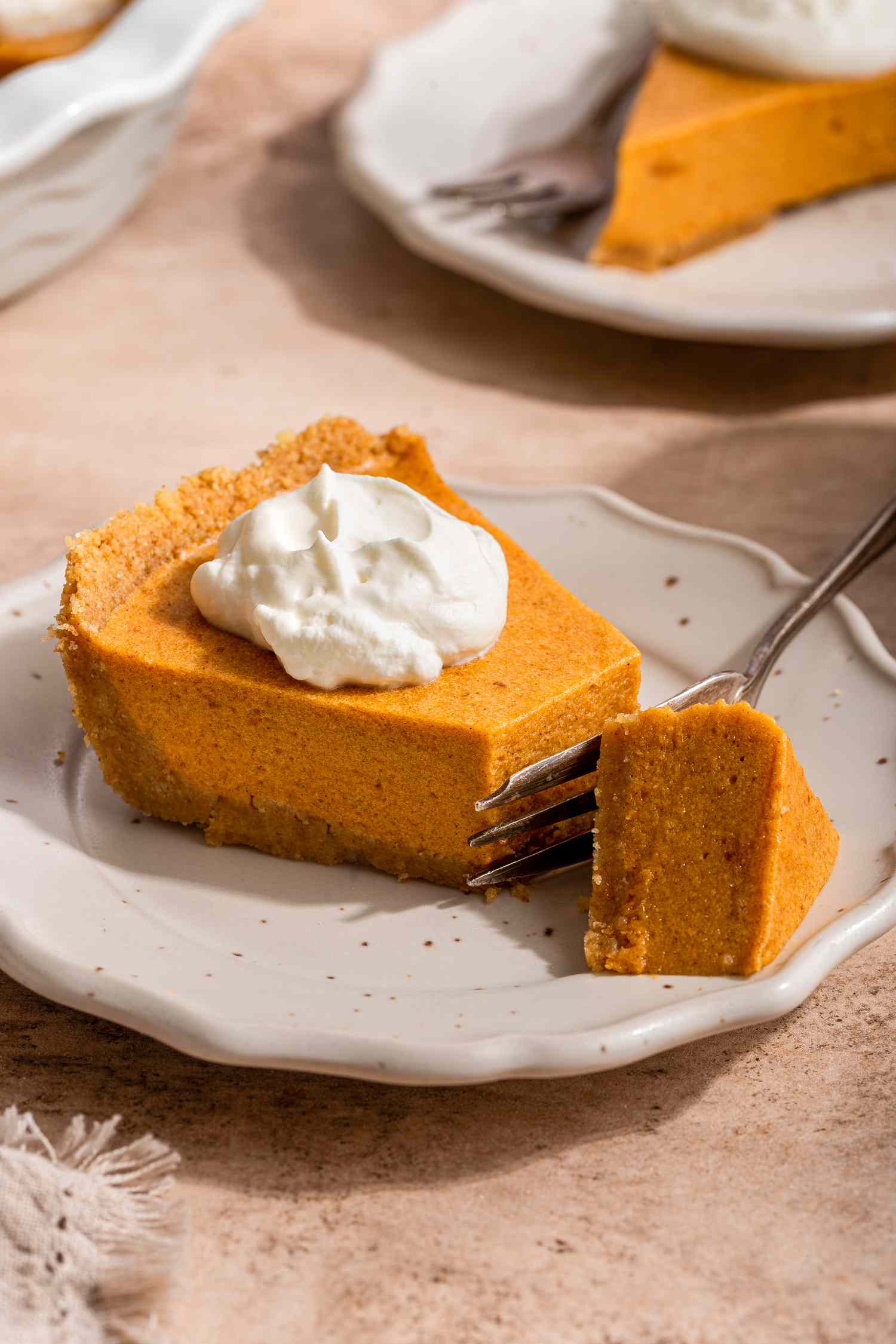 Slice of no-bake pumpkin pie on a plate with cut into using a fork, and in the background, another slice of pumpkin pie