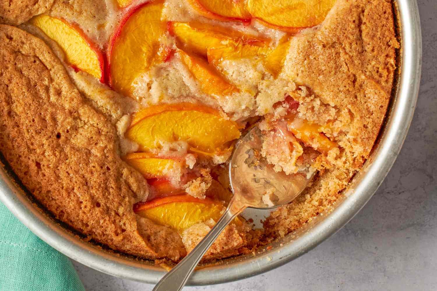 Peach dessert in a round pan with a spoon scooping a portion