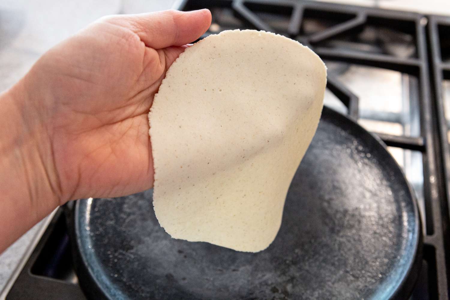 A hand setting a tortilla in a hot skillet