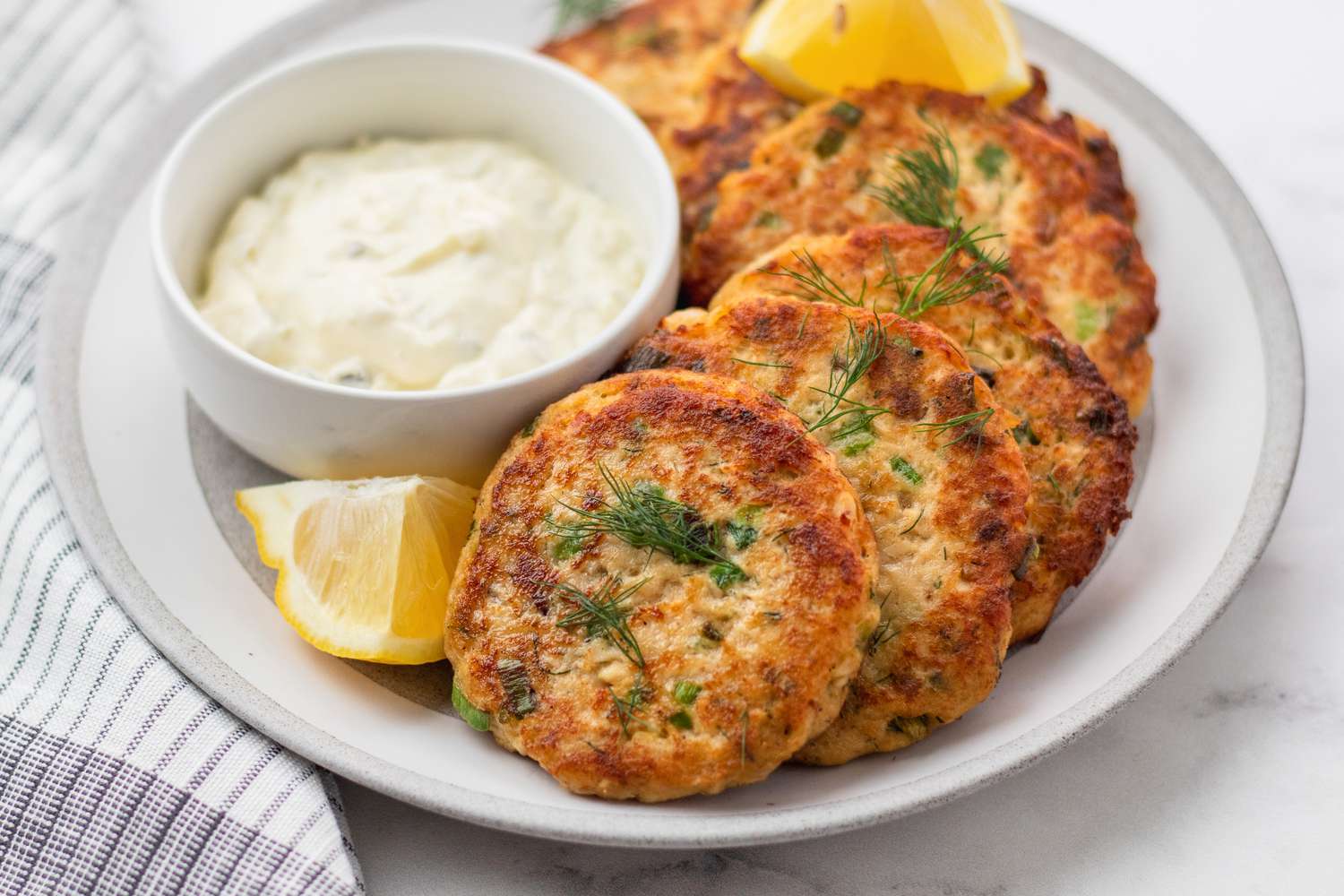 Salmon patties set on a plate with a dip and lemon.