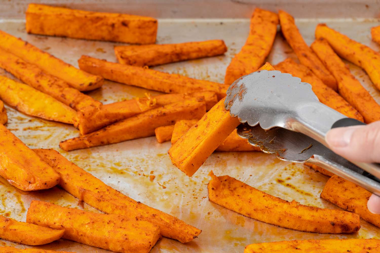 Sweet potato fries on a baking sheet being flipped with tongs 