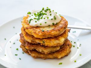 Leftover mashed potato pancakes stacked on a plate and topped with sour cream and chives.