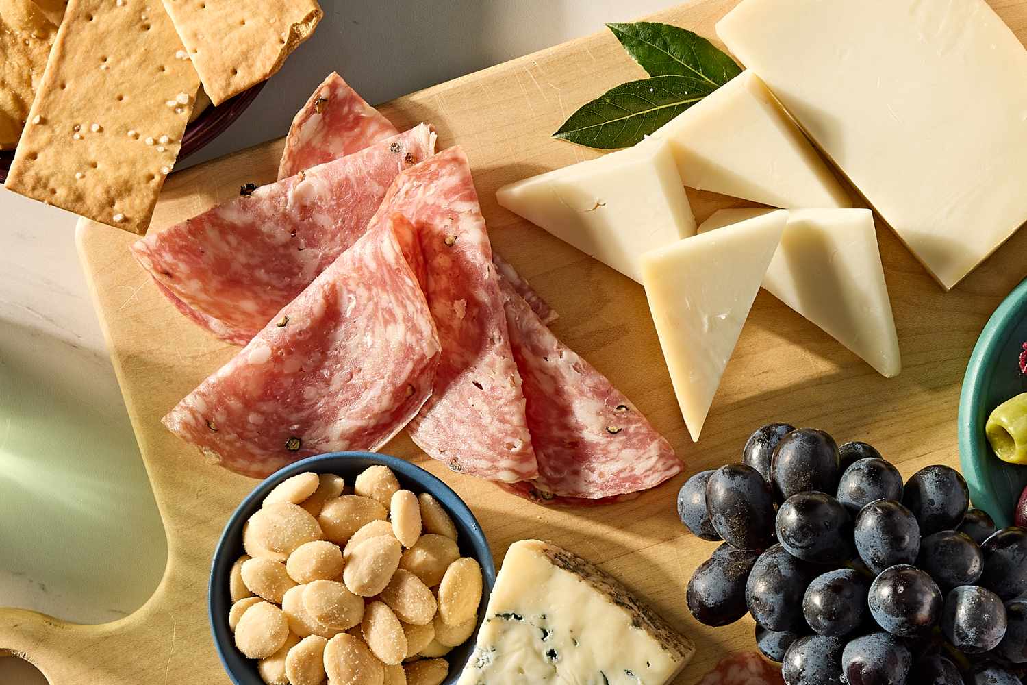 Charcuterie board featuring sliced salami wedges of cheese crackers almonds and grapes