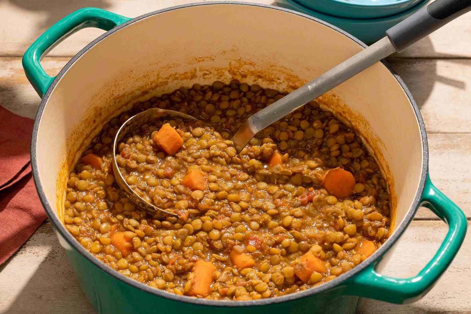 A pot of spiced lentils with cubes of vegetables and a ladle inside