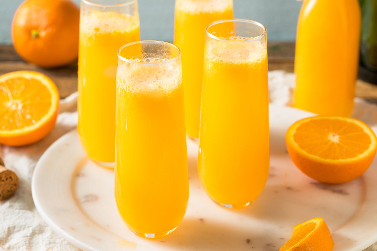 Side view of four tall glasses of Mimosa cocktails on a plate with sliced oranges
