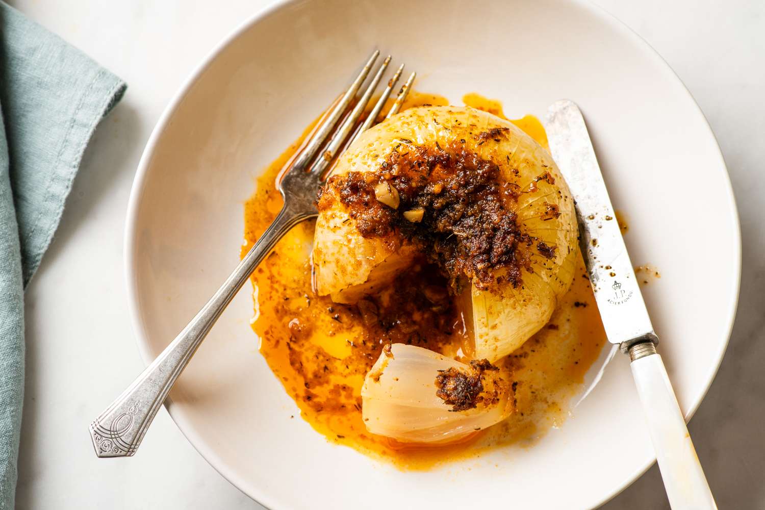 Whole cooked onion cut open served with sauce on a plate with a knife and fork
