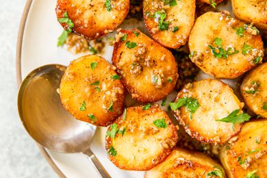 Garlic-coated roasted potatoes topped with fresh herbs on a plate with a spoon
