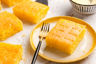 Angled view of a slice of orange poke cake and fork on a white and yellow plate with four slices of cake to the side along with a bowl of glaze