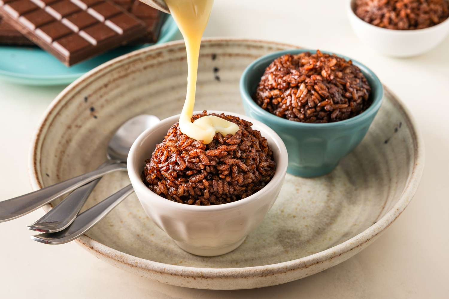 Two bowls of chocolate rice pudding one being topped with creamery sauce placed on a dish with utensils
