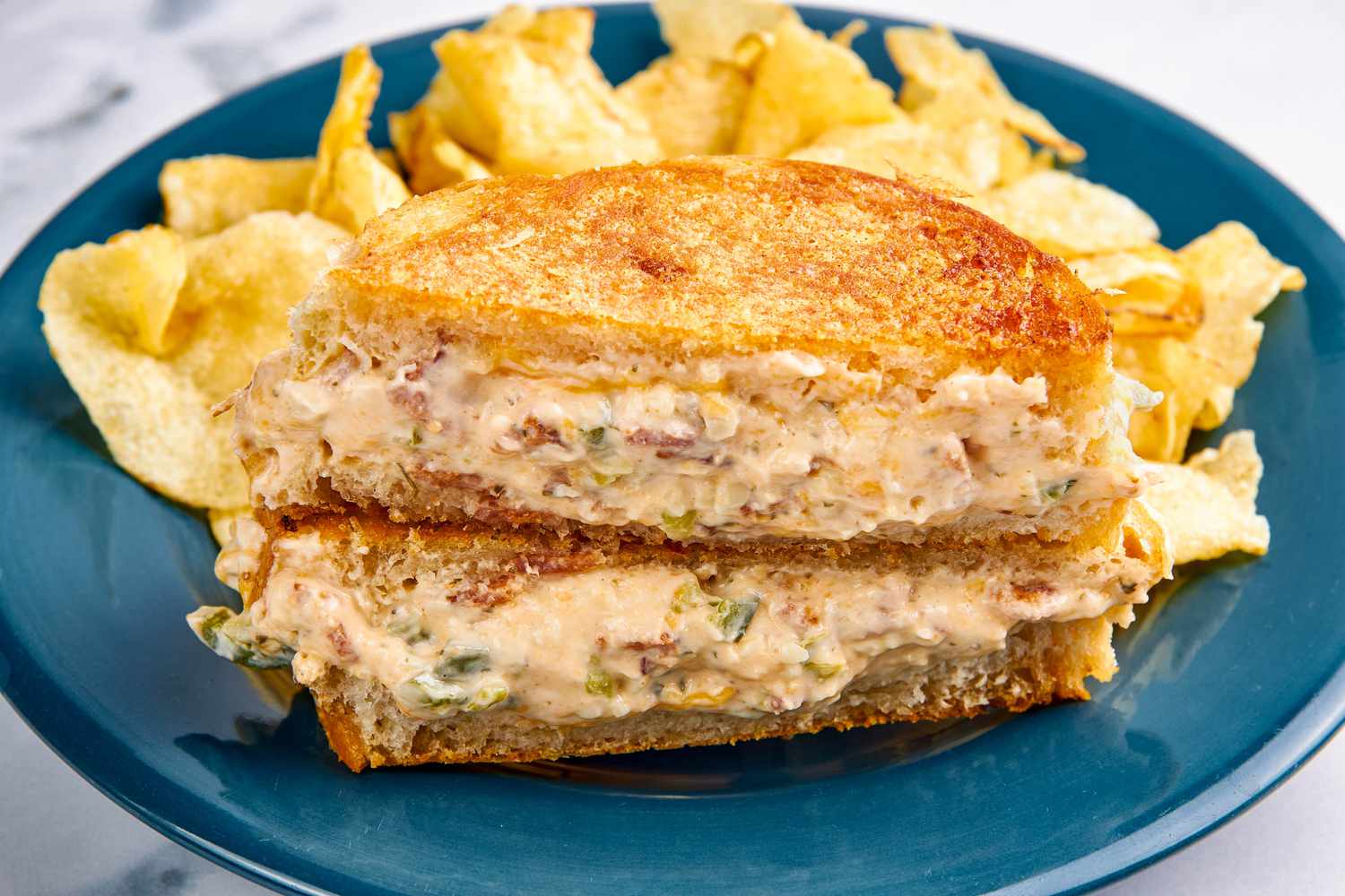 Plate with jalapeno popper grilled cheese (cut in half diagonally and stacked to showcase a cross-section) served with kettle chips