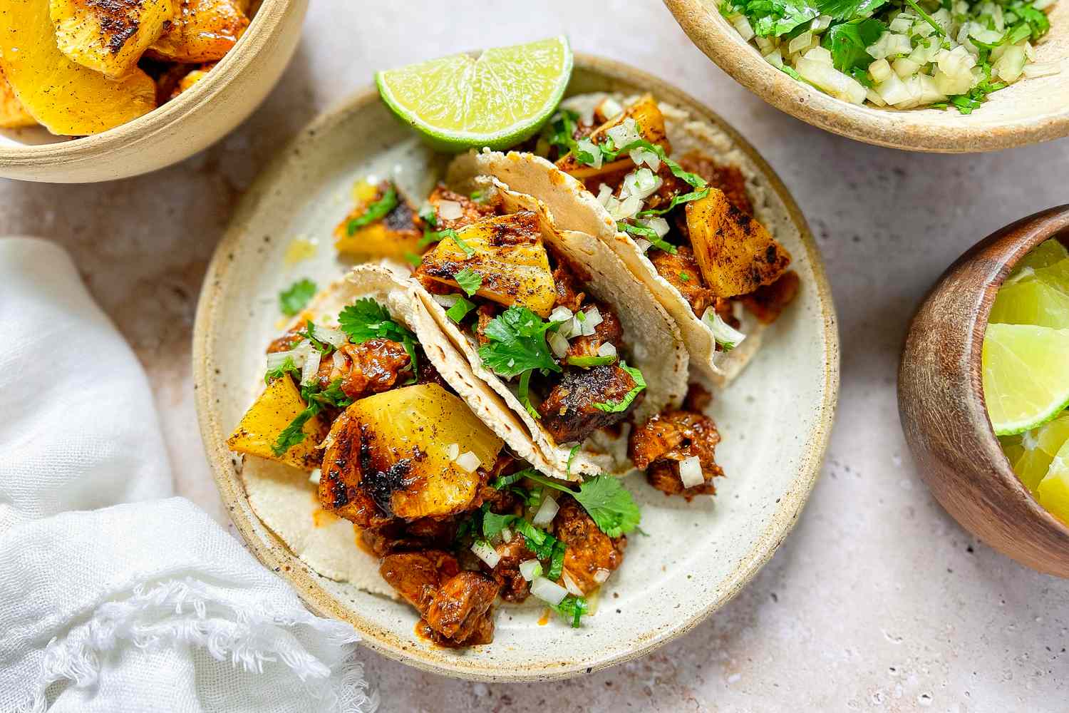 Plate of Tacos al Pastor with Pork, Pineapple, Cilantro, and a Lime Wedge Surrounded by Additional Taco Ingredients
