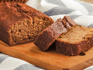 A loaf of spice cake on a wooden board partially sliced with two pieces visible