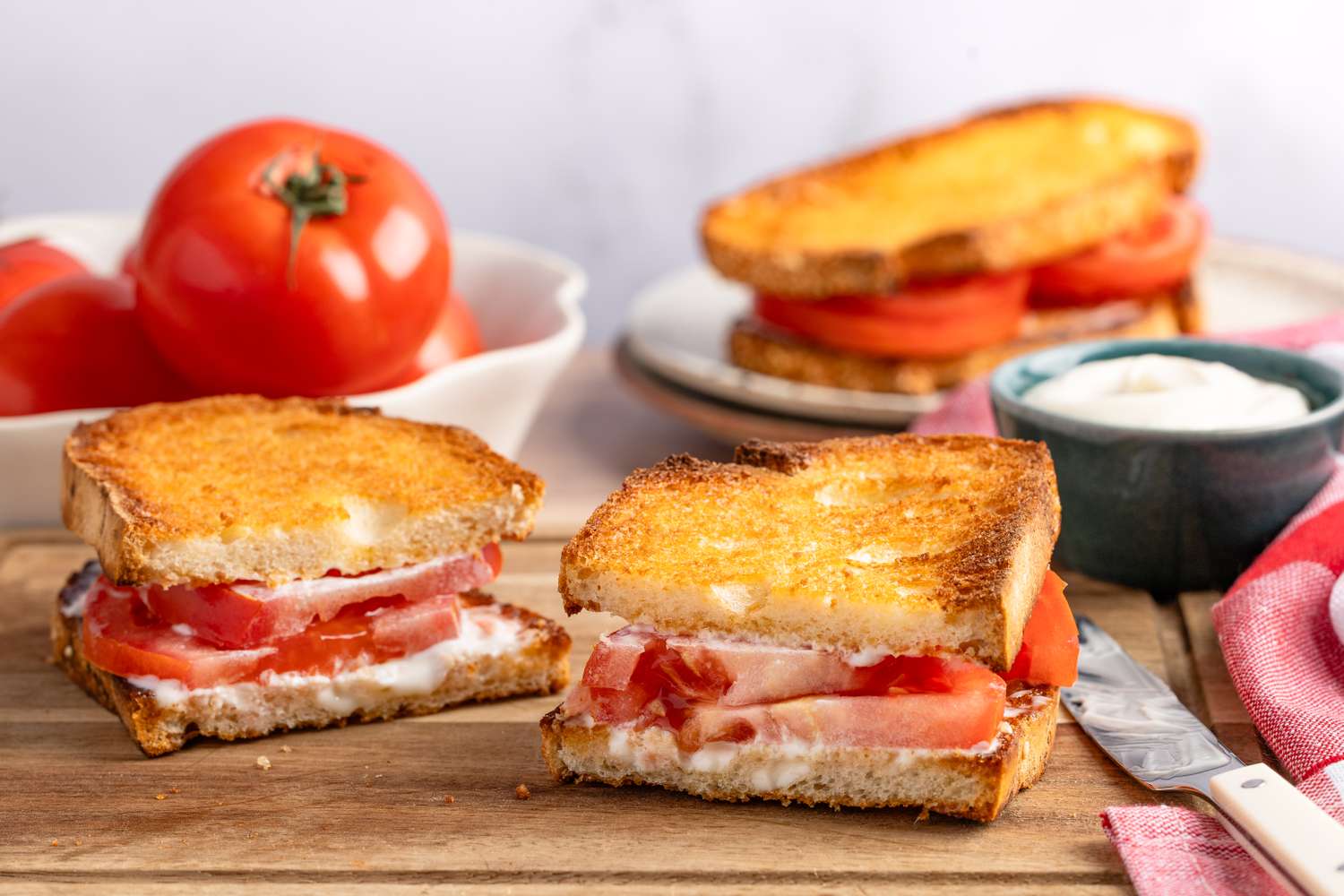 Sliced tomato sandwich on toasted bread with spread on a wooden surface
