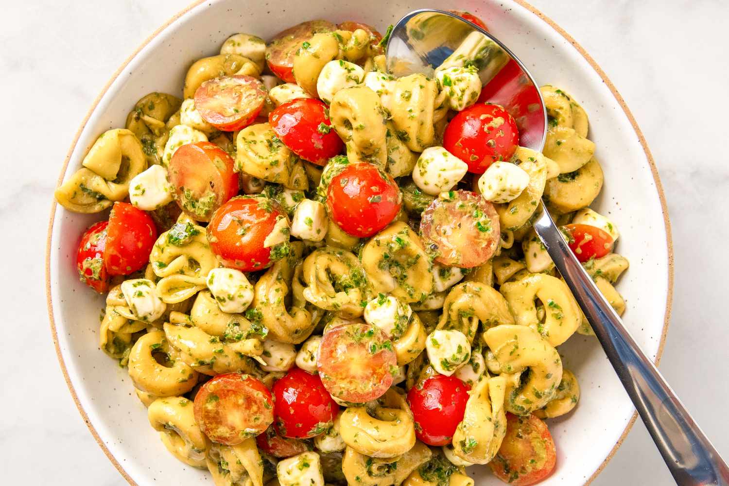 A bowl of tortellini salad with pesto, cherry tomatoes, and mozzarella