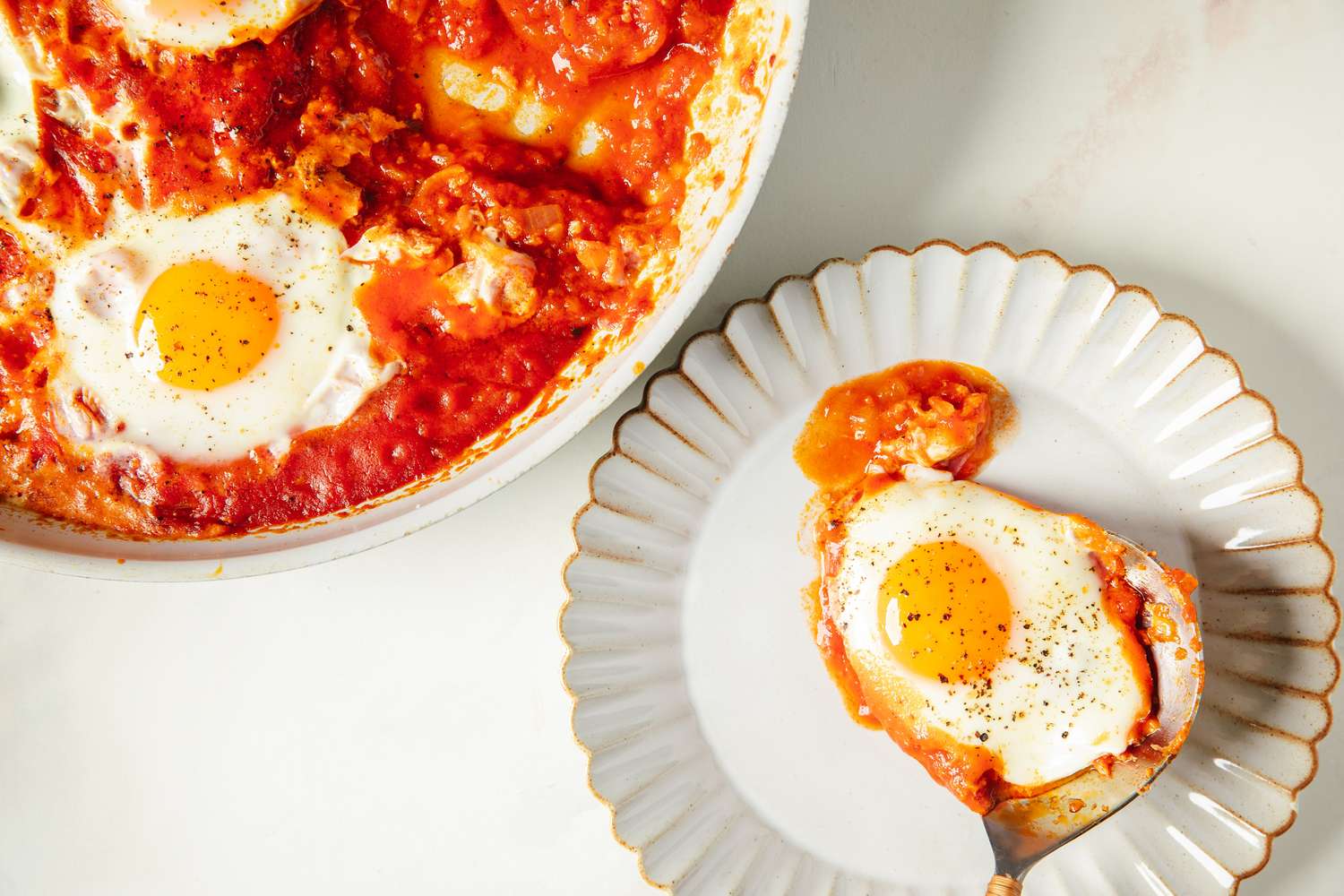 Eggs cooked in tomato sauce served in a skillet and on a plate with a spoon