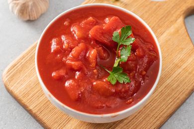 A bowl of canned tomatoes garnished with parsley on a wooden board