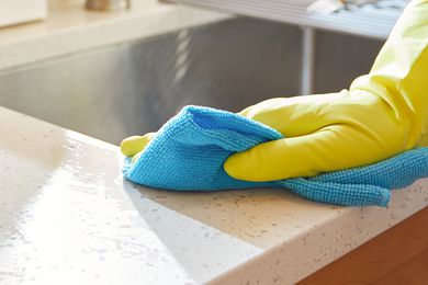 A house cleaner cleaning and sanitizing kitchen worktop and surfaces wearing rubber gloves and using a blue towel