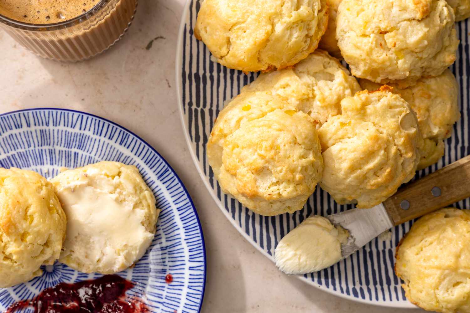 Overhead view of a plate with one sliced mashed potato biscuit with butter next to a plate of more biscuits ready to serve