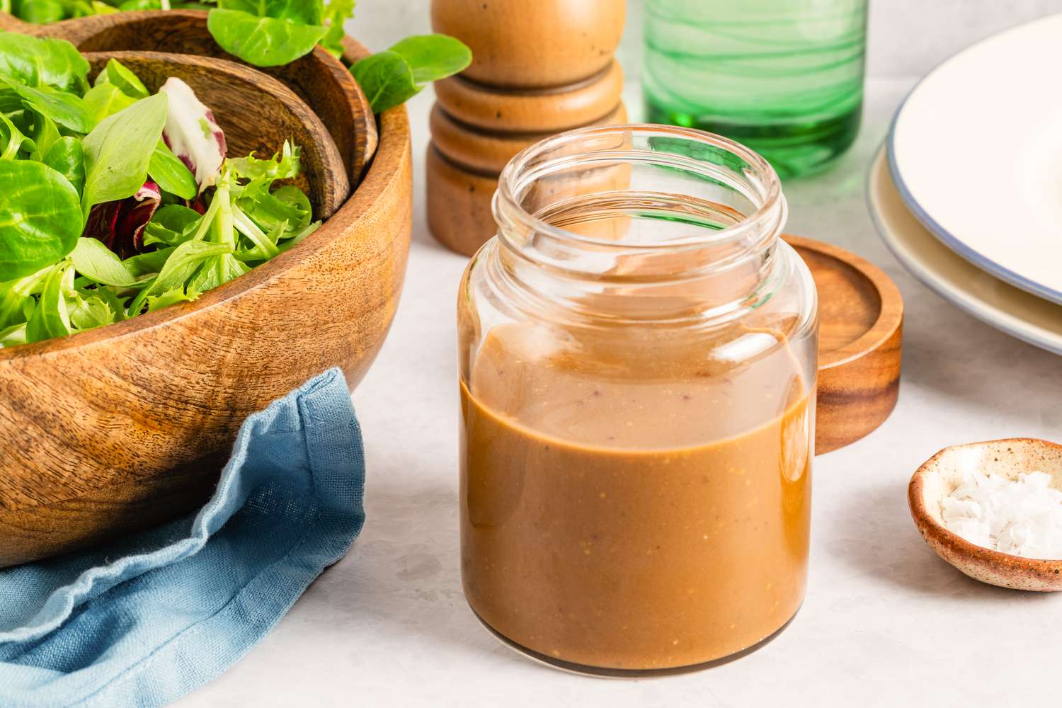 Jar of salad dressing placed on a table with a bowl of greens in the background