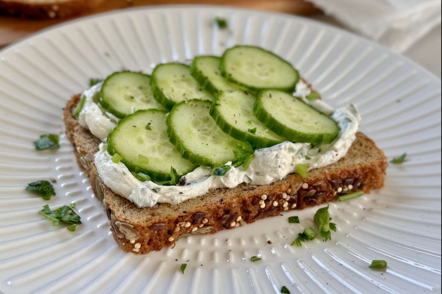 Openfaced sandwich with cucumber slices on herbed cream cheese atop wholegrain bread